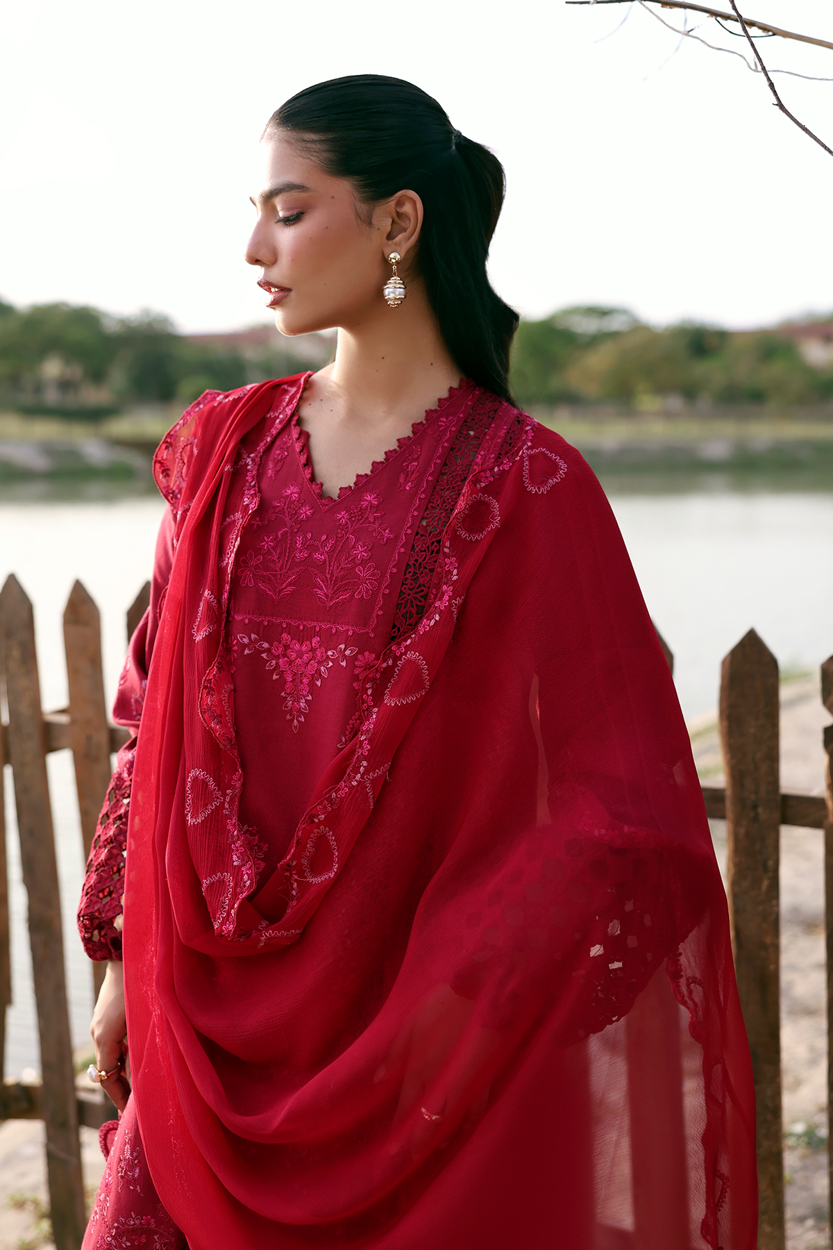 Woman in a red traditional outfit standing by a lake with trees in the background