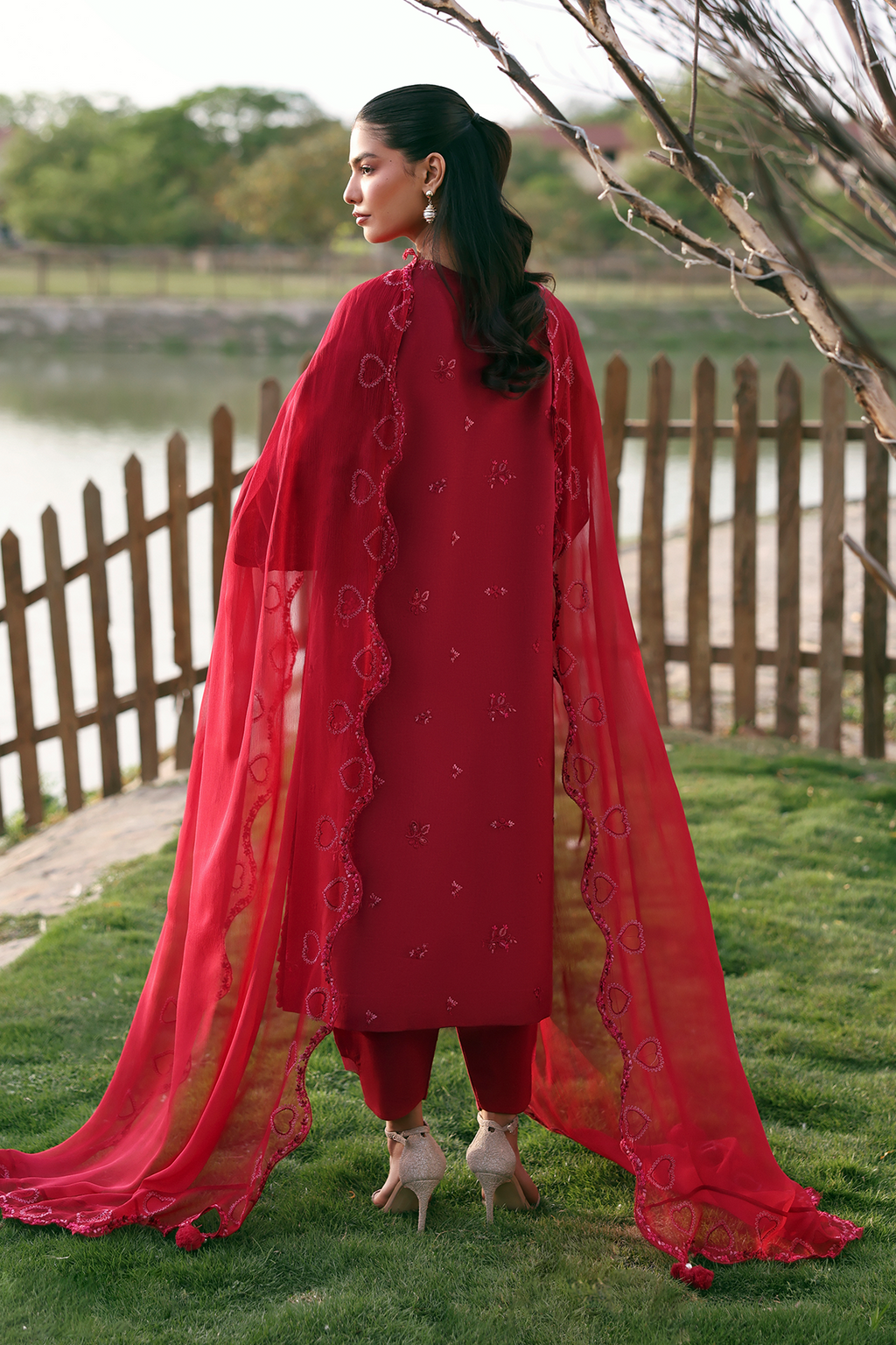 Woman in a red traditional outfit standing outdoors by a lake