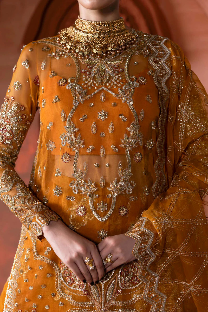 A close-up of a model wearing a rich mustard yellow traditional outfit with intricate gold embroidery, beadwork, and a matching sheer dupatta against a warm, softly lit background.