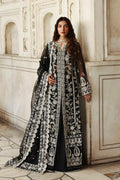 Woman in a black and white embroidered traditional outfit standing against a white marble wall.
