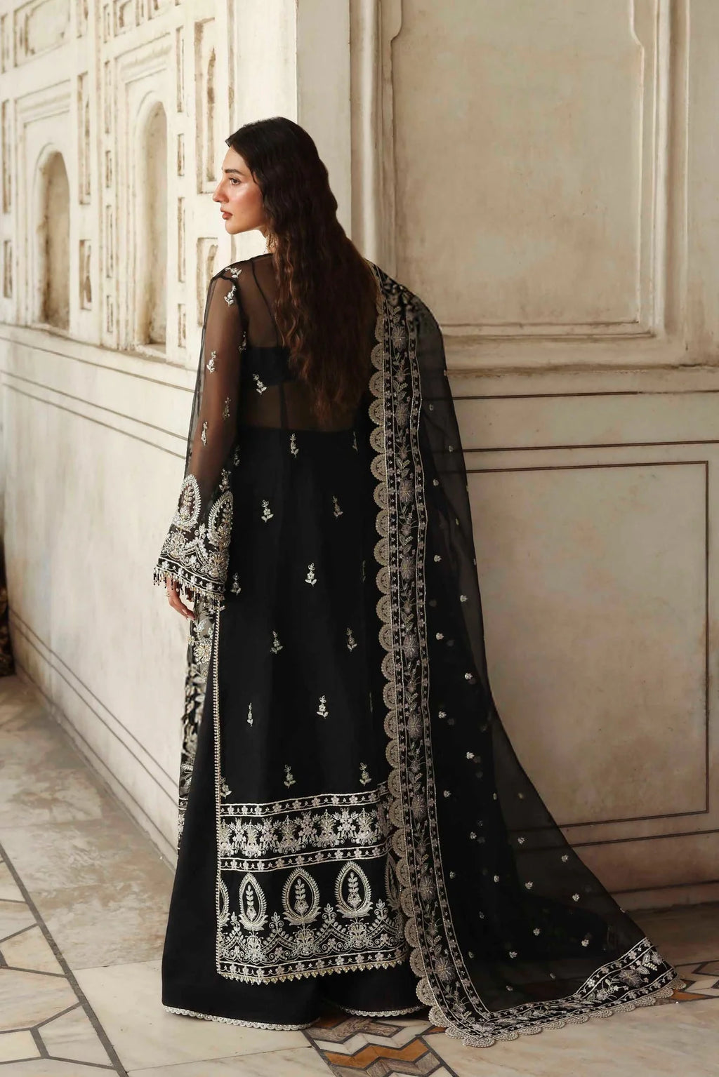 Woman wearing a black traditional outfit with white embroidery in an elegant interior setting.