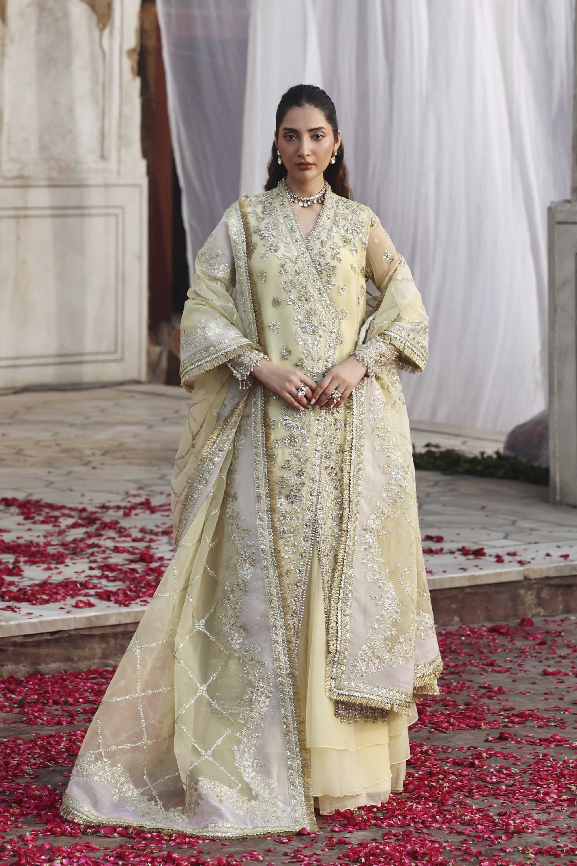 Woman in a traditional outfit standing on a path with rose petals, surrounded by white curtains.