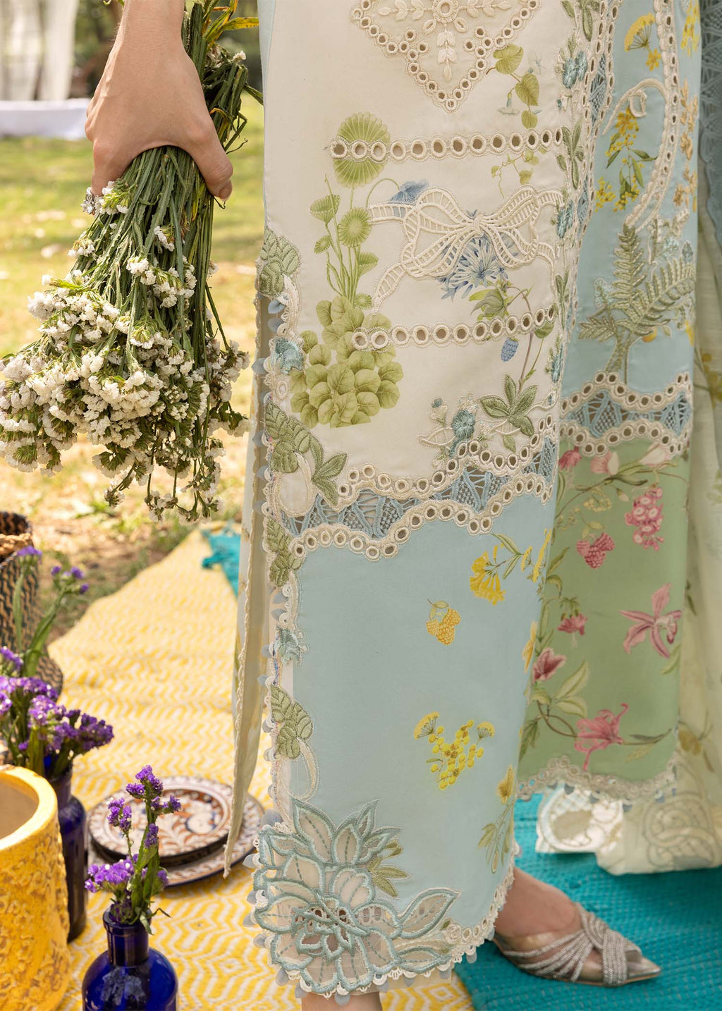 Person wearing a floral embroidered dress holding a bouquet of flowers outdoors.