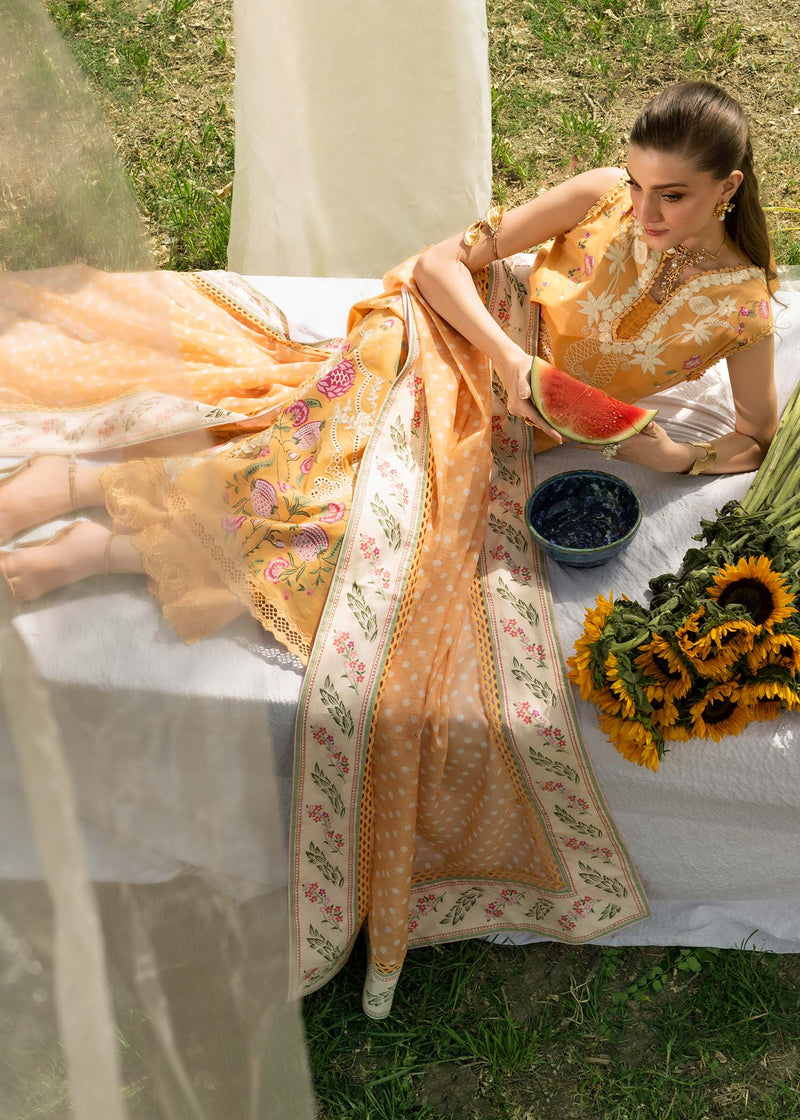 Woman in a floral dress sitting at a table with a bowl of fruit and flowers outdoors.