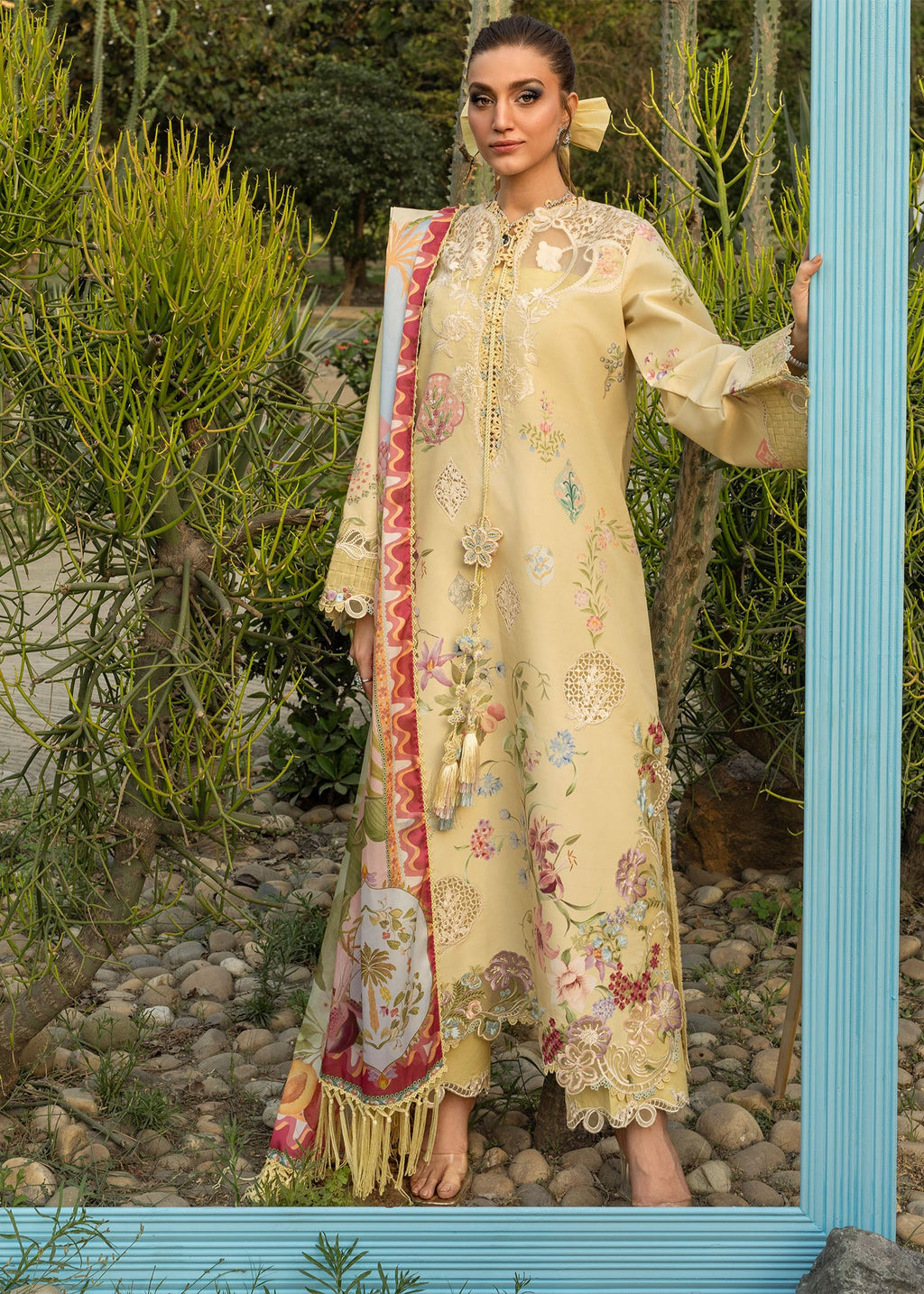 Woman wearing a beige embroidered outfit with a floral shawl in a natural setting.