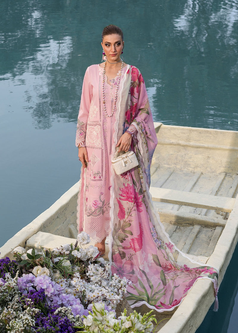 Woman in a pink floral dress standing in a boat with flowers by a body of water.