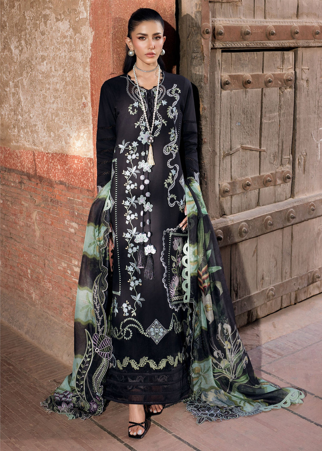 Woman in an embroidered black and green dress standing in front of a rustic wooden door.