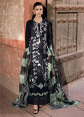 Woman in an embroidered black and green dress standing in front of a rustic wooden door.