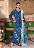 Woman in a blue embroidered outfit standing in front of a decorative wall.