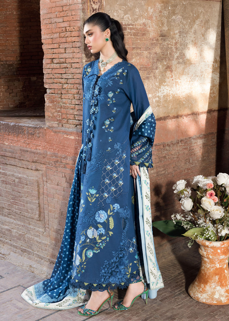 Woman in a blue embroidered outfit standing against a brick wall with flowers.
