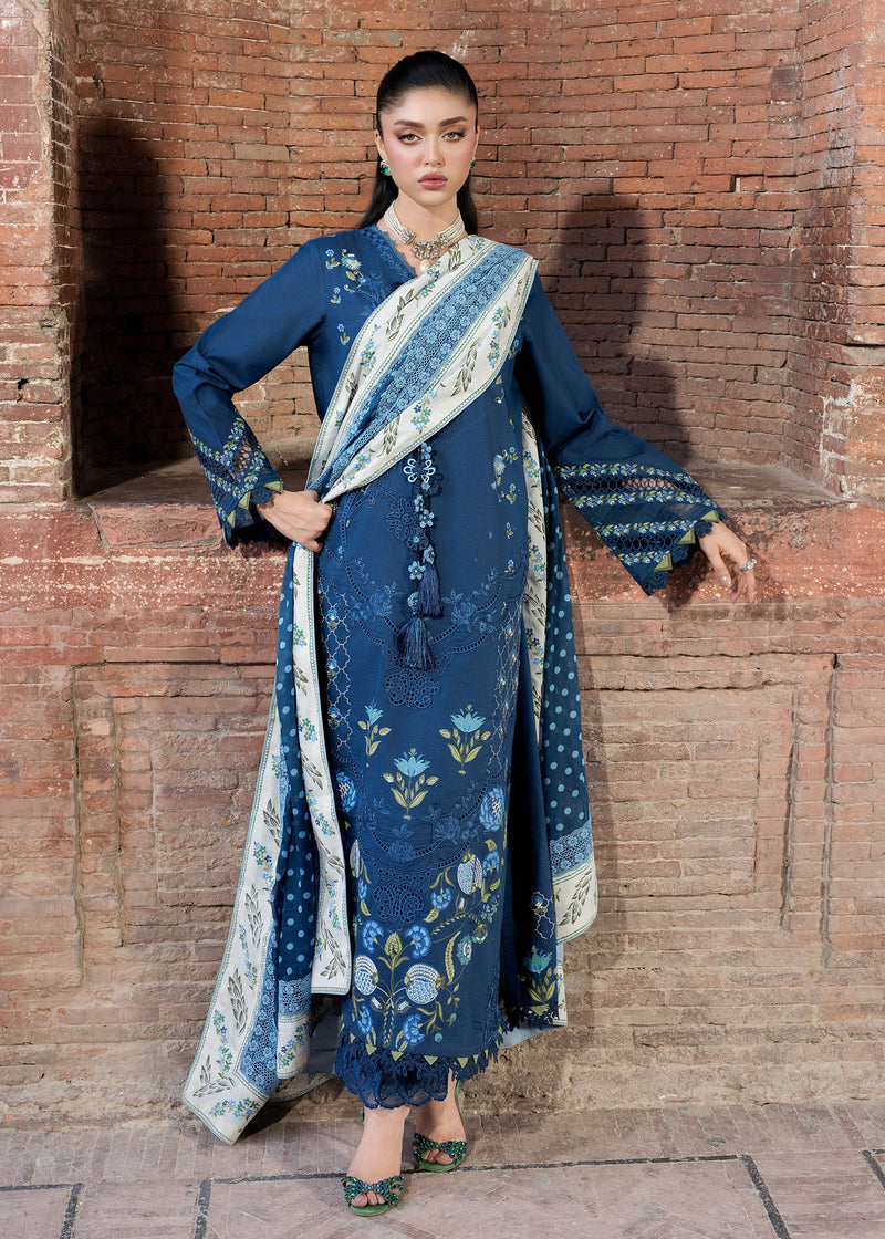Woman in a blue embroidered outfit standing against a brick wall.