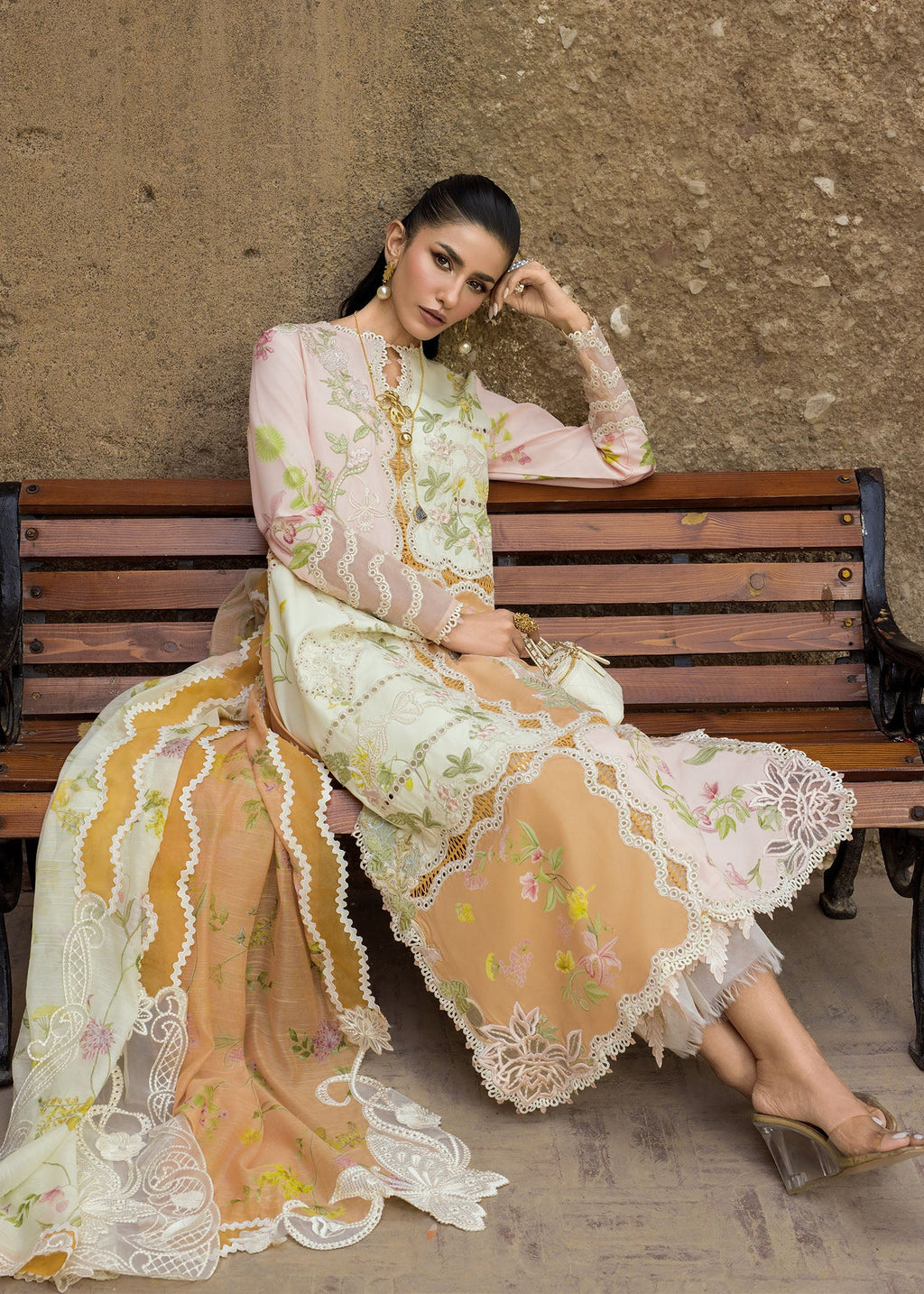 Woman in a floral dress sitting on a wooden bench against a textured wall.