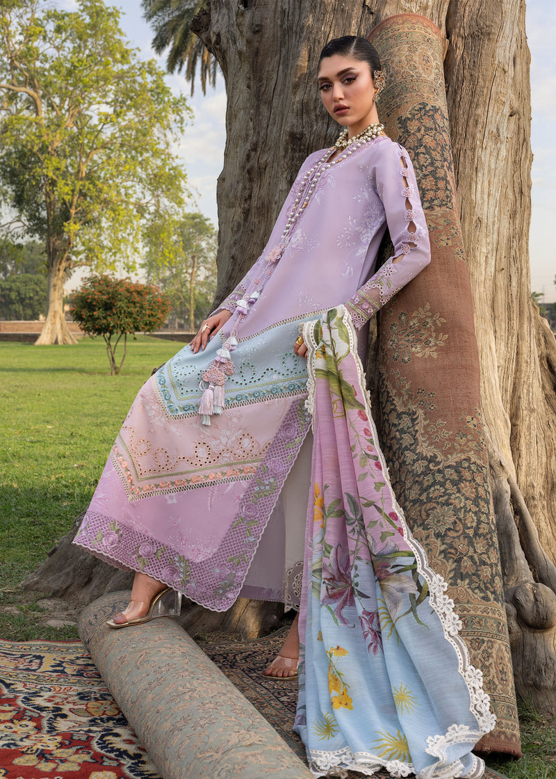 Woman in a light purple and blue traditional outfit leaning against a tree in a park.