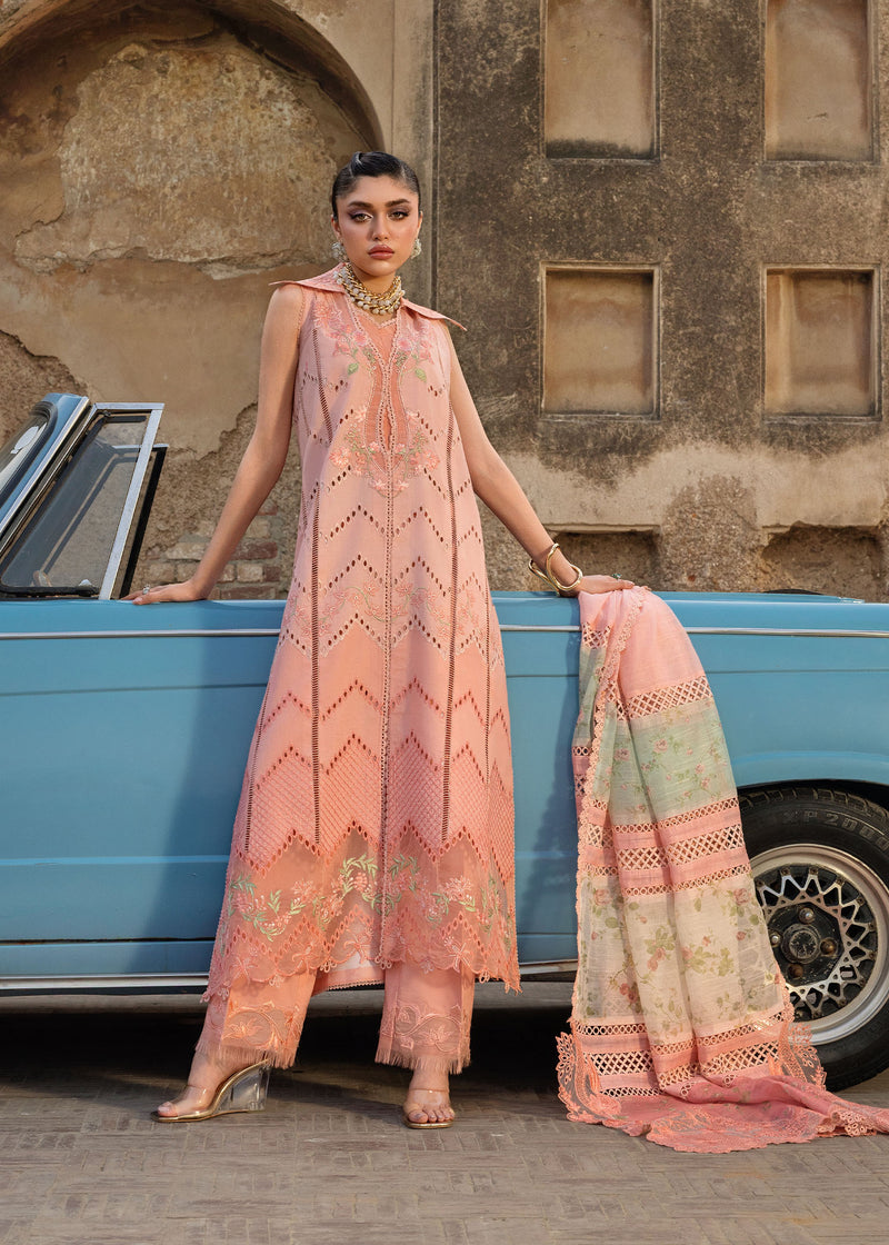 Woman in a pink embroidered dress standing next to a blue car with a textured wall background
