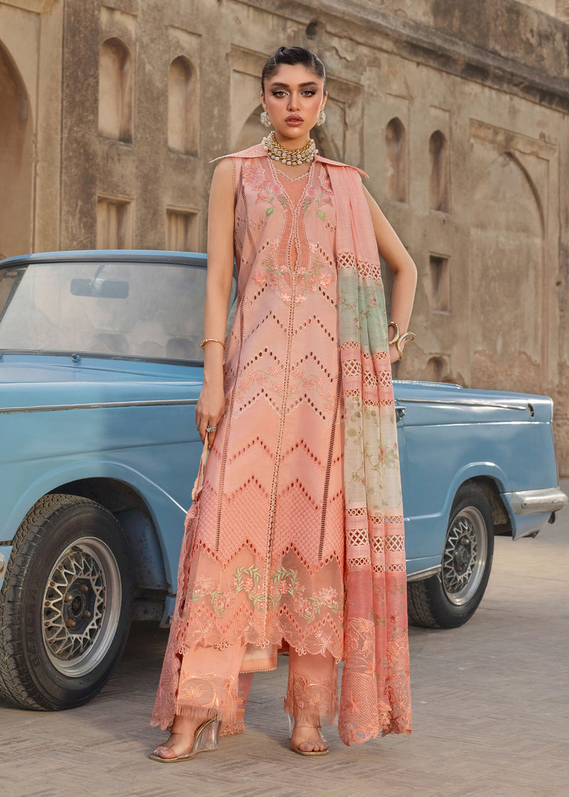 Woman in a peach embroidered outfit standing next to a vintage blue car with a stone building in the background.