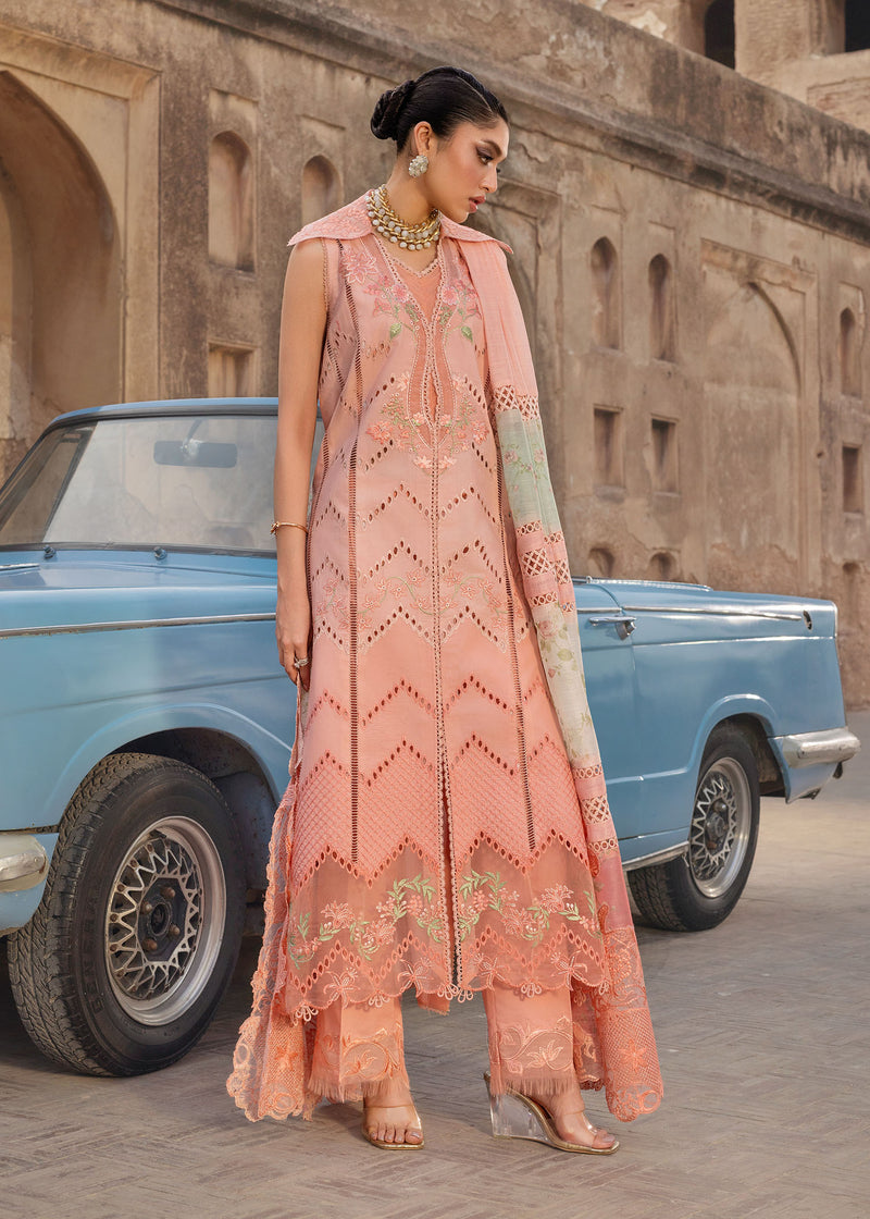 Woman in a peach embroidered outfit standing next to a vintage blue car with a stone building in the background