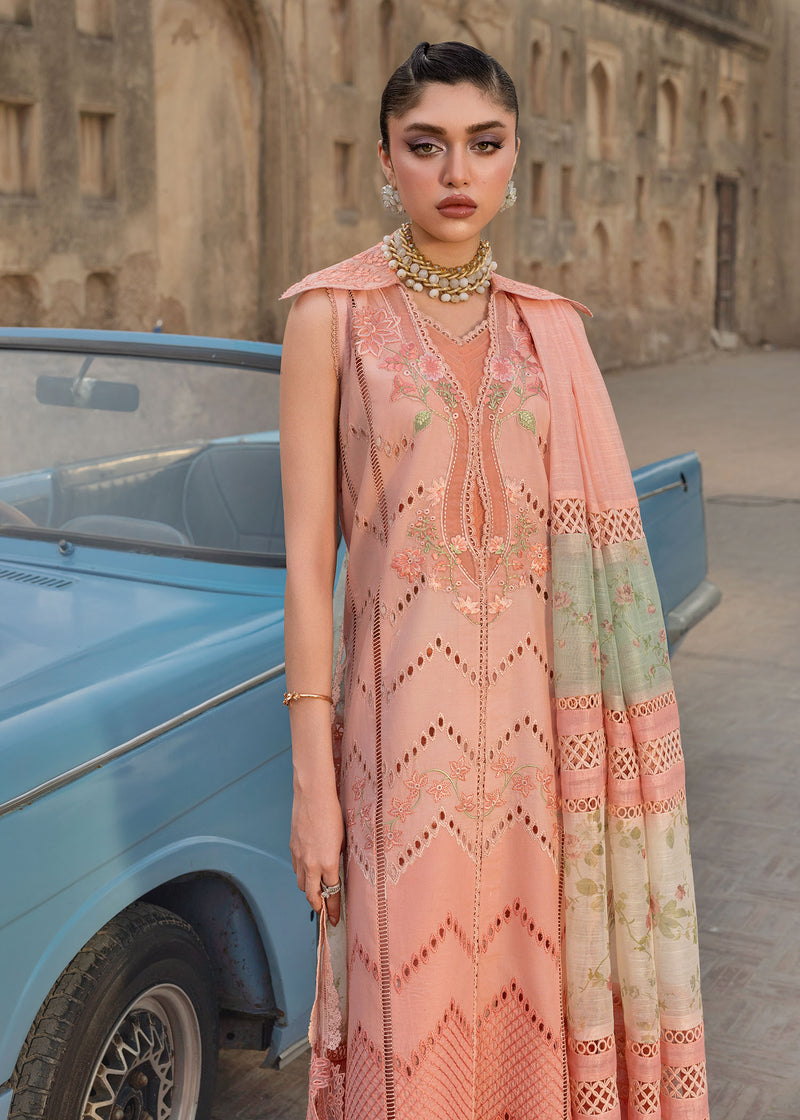 Woman in a peach embroidered outfit standing next to a blue car with a stone building in the background