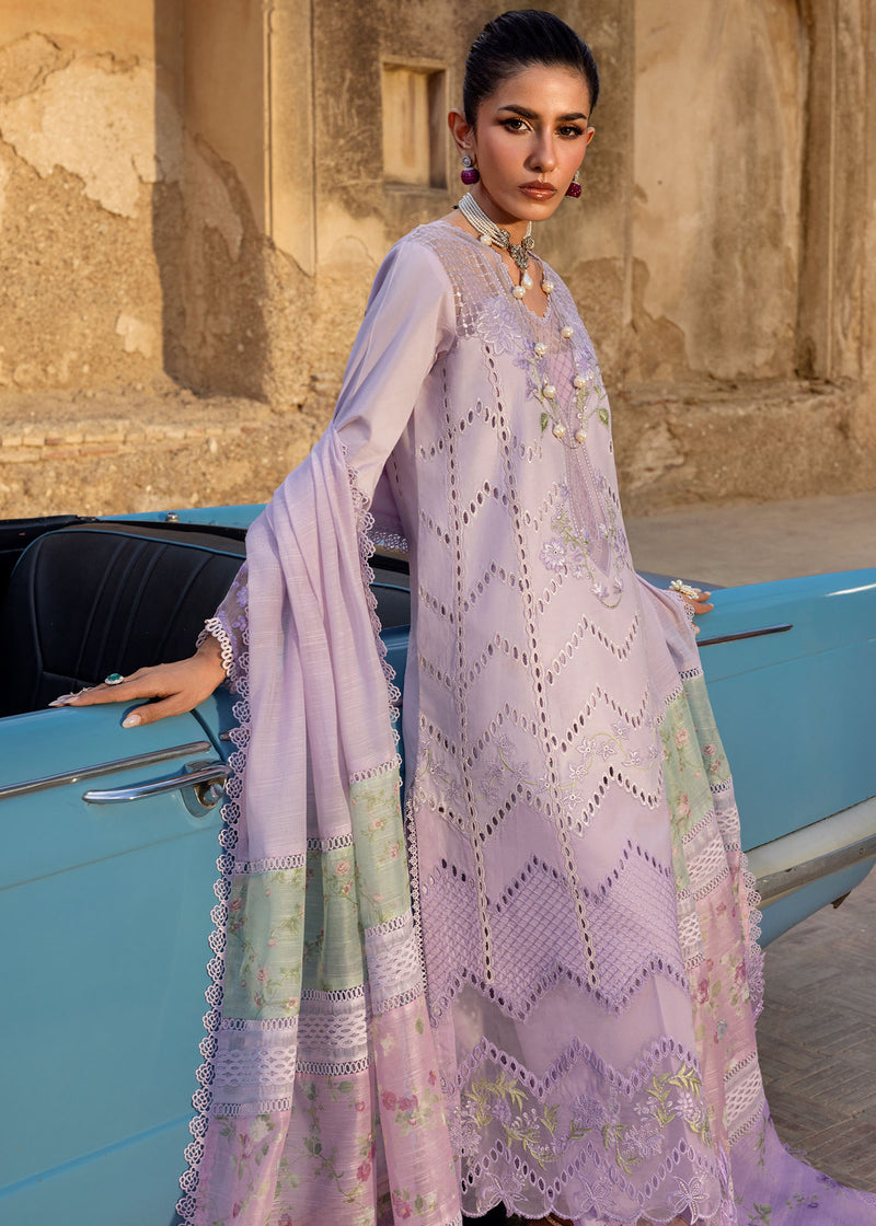 Woman in a light purple embroidered outfit standing next to a vintage blue car with an architectural background.