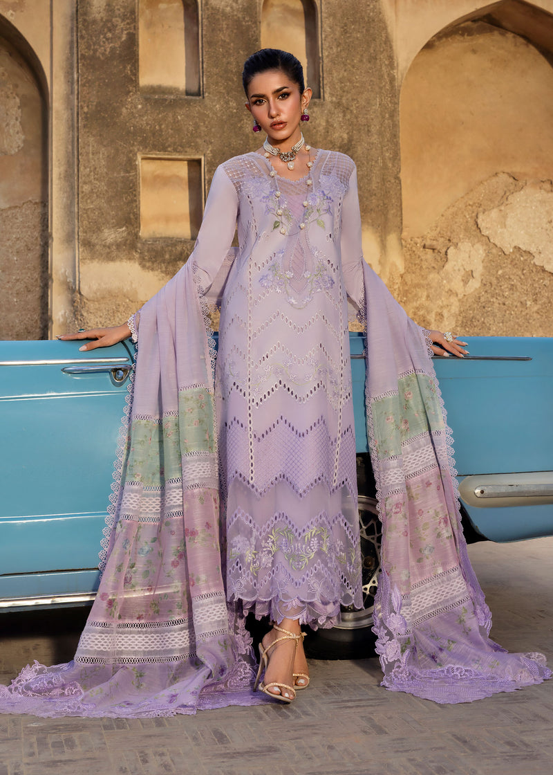 Woman in a lavender embroidered outfit standing next to a vintage blue car with a beige building in the background.