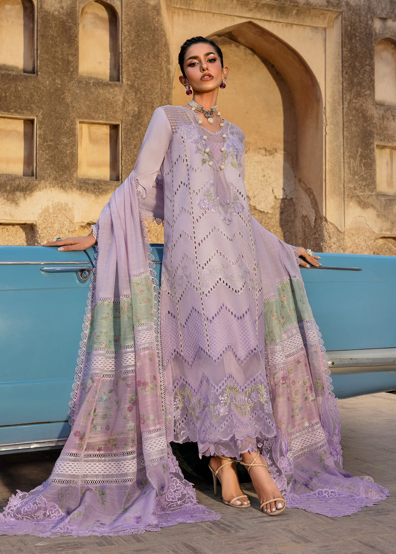 Woman in a lavender embroidered outfit standing next to a vintage blue car with an archway in the background.