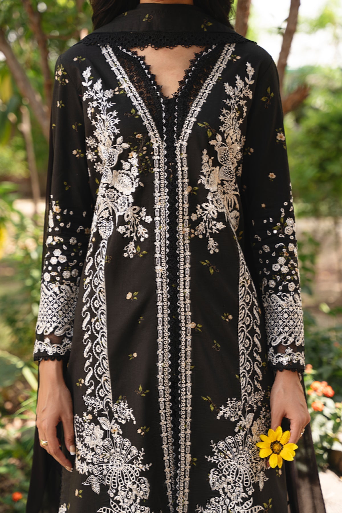 Black dress with white floral embroidery held by a person in a garden setting