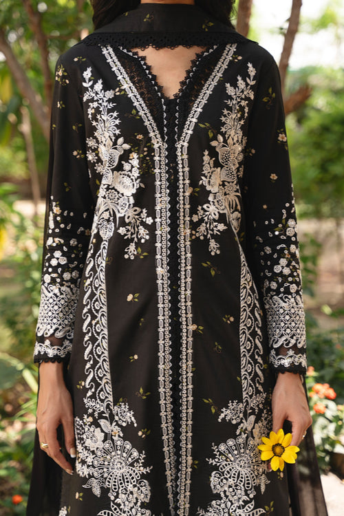 Black dress with white floral embroidery held by a person in a garden setting