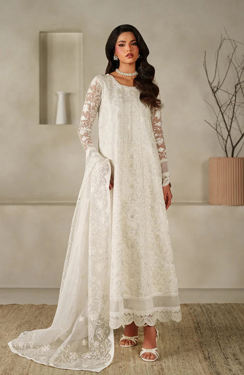 Woman wearing a white embroidered traditional outfit in a minimalistic room.