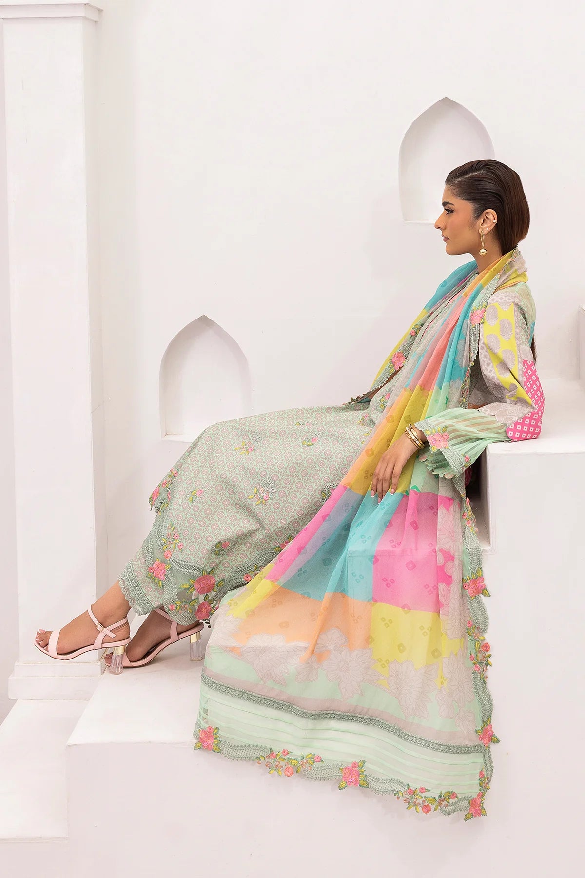 Woman in a pastel-colored traditional outfit with a colorful dupatta sitting on a white surface.