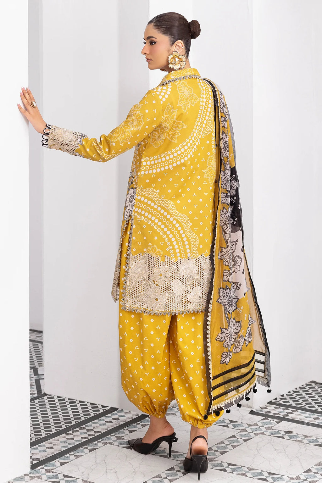 Woman wearing a yellow traditional outfit with a black and white dupatta in a white room.