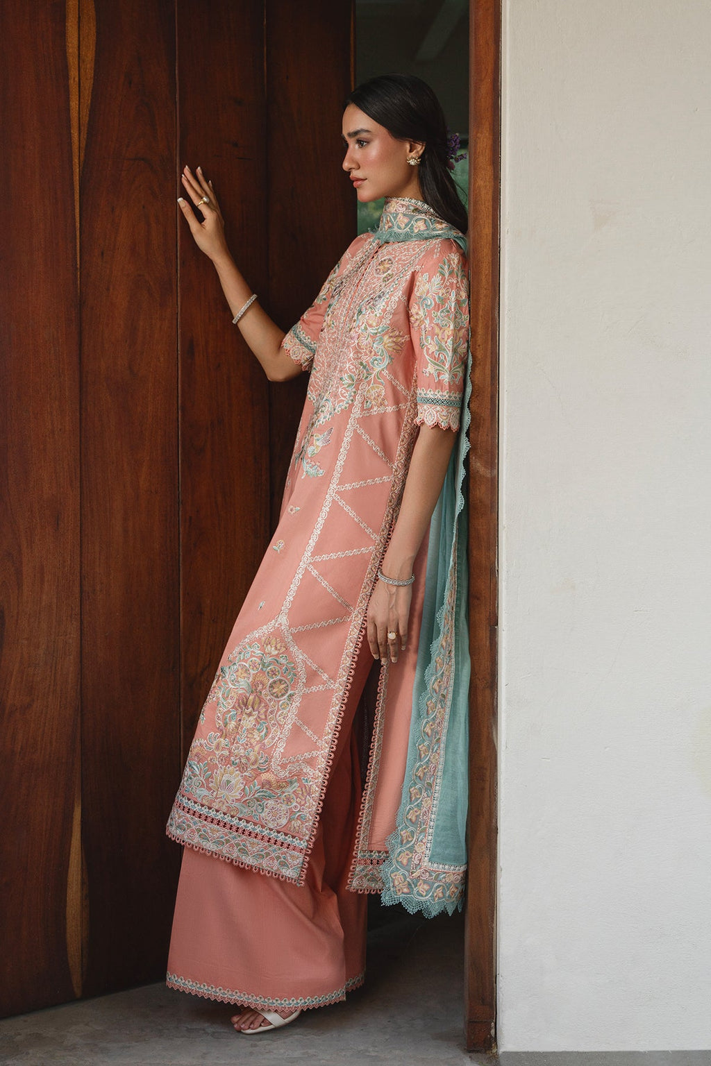 Woman in a traditional pink and blue embroidered outfit standing in a doorway.