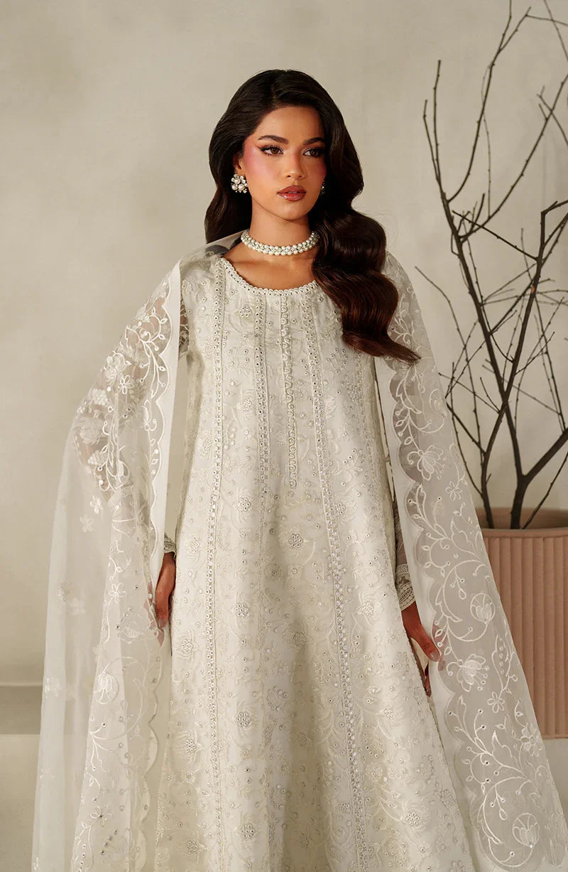 Woman wearing a white embroidered dress with a cape against a neutral background