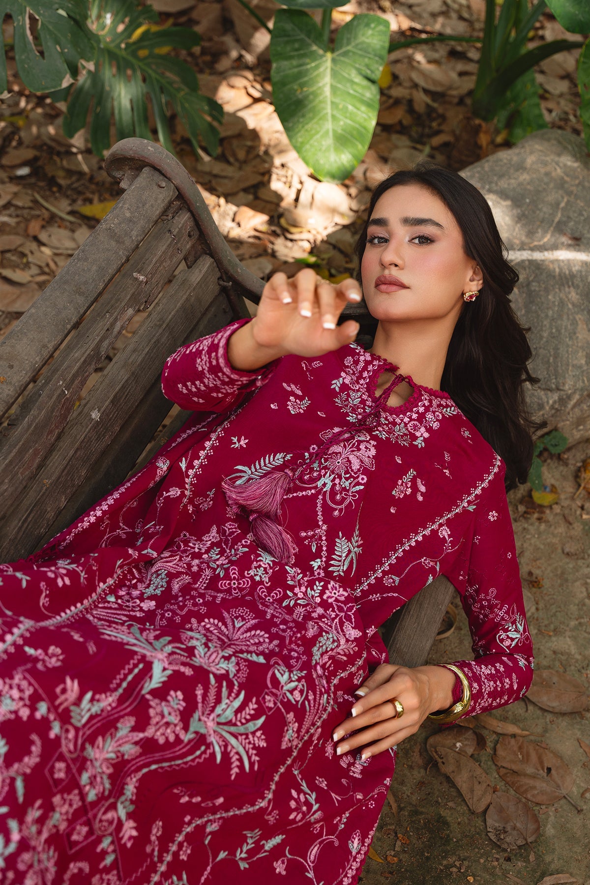 Woman in a red floral dress sitting on a wooden bench outdoors.