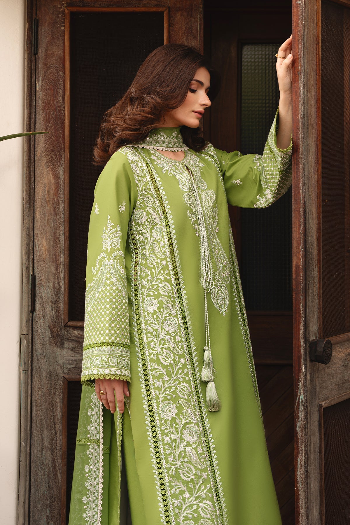 Woman wearing a green embroidered traditional outfit standing in front of a wooden door.