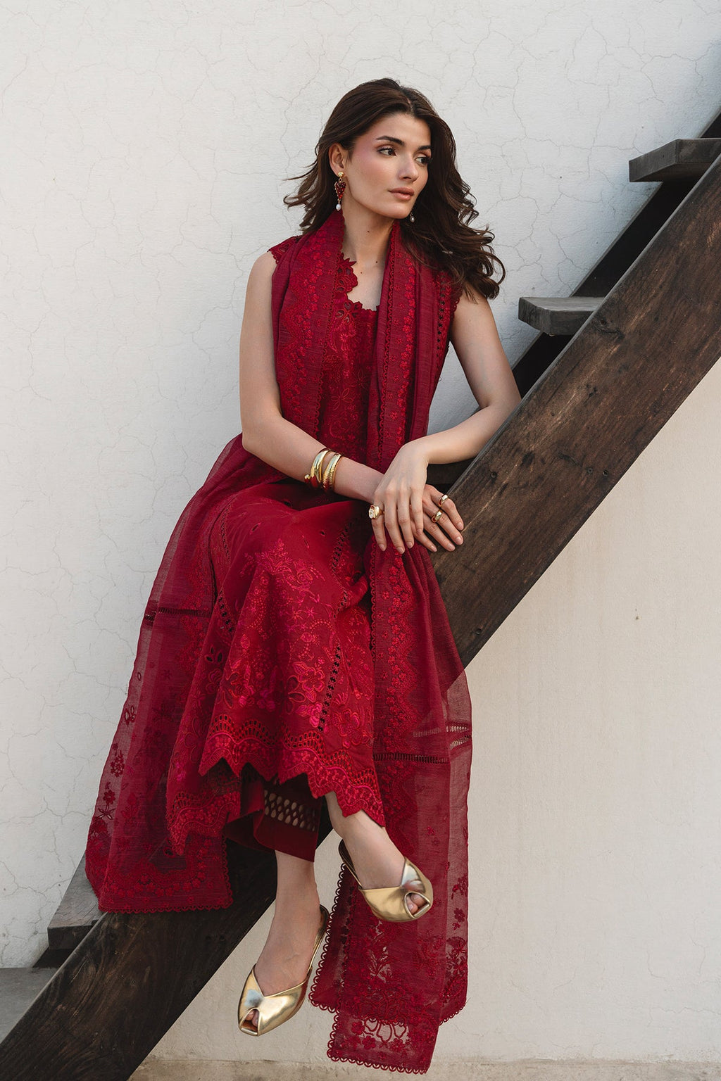Woman in a red dress sitting on a wooden staircase against a white wall.