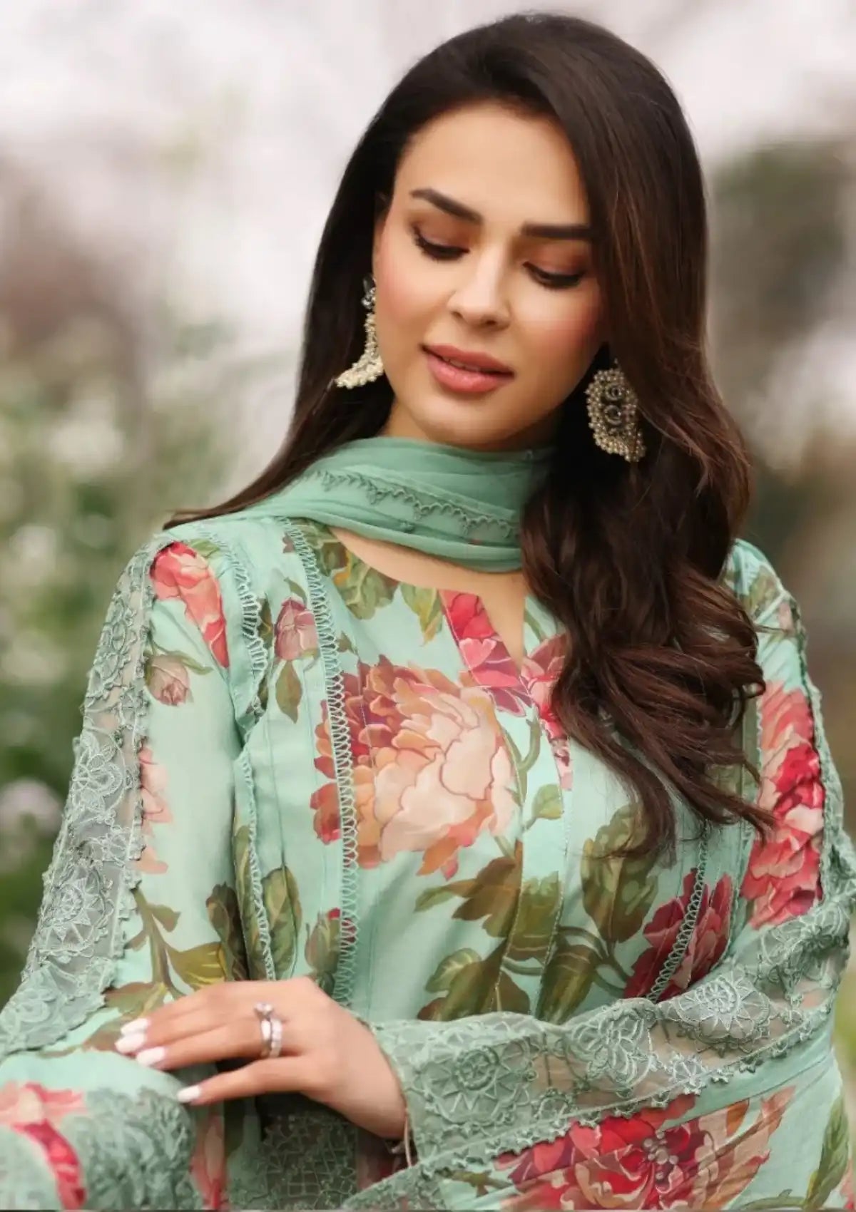 A woman wearing a mint green floral printed traditional outfit with lace sleeves and a matching scarf, photographed outdoors against a softly blurred background.