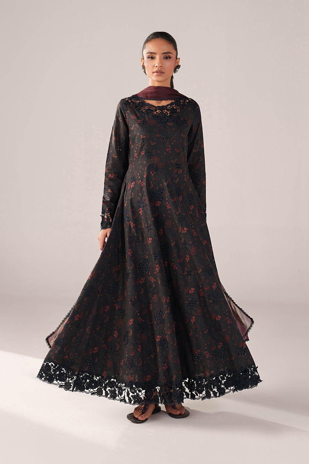 Woman wearing a long black dress with floral patterns on a plain background