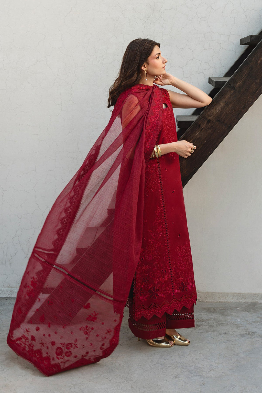 Woman in a red traditional outfit with a sheer dupatta standing on a staircase.