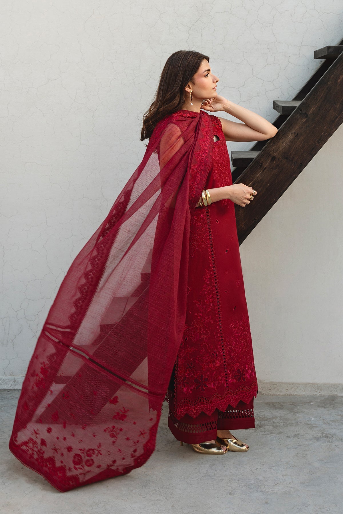 Woman in a red traditional outfit with a sheer dupatta standing on a staircase.