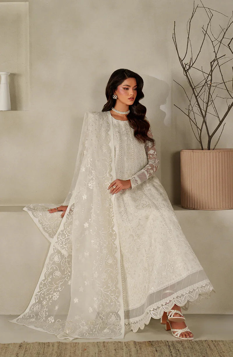 Woman in a white embroidered traditional outfit standing indoors with a neutral background