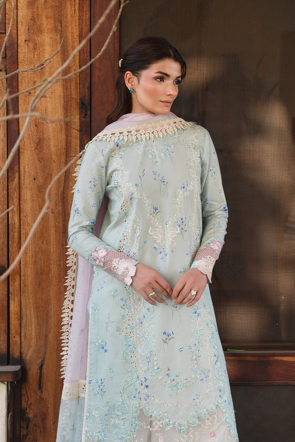 Woman wearing a light blue embroidered traditional outfit with a wooden background