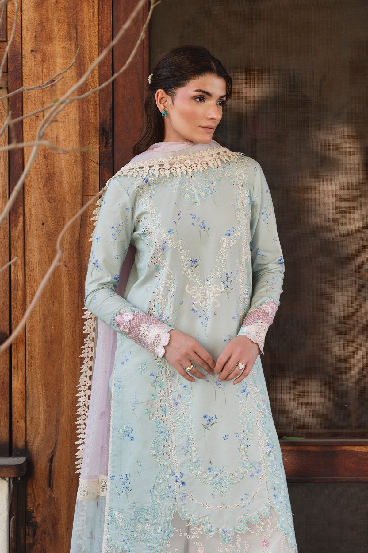 Woman wearing a light blue embroidered traditional outfit with a wooden background