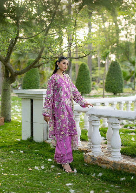 Woman in a pink traditional outfit standing in a garden with greenery and a white railing.