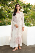 Woman wearing a light-colored embroidered outfit standing outdoors with greenery in the background