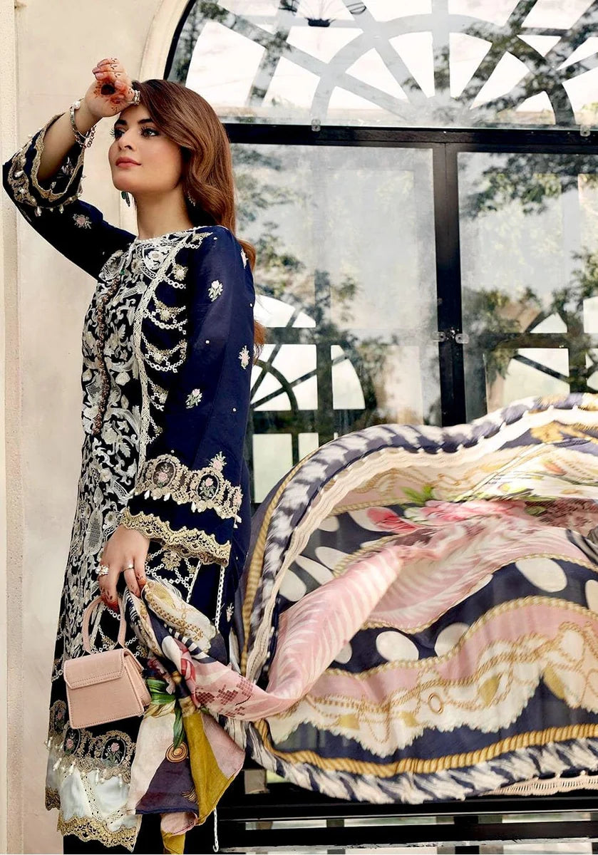 A woman models a navy blue and silver embroidered traditional outfit with a matching patterned scarf and a small light pink handbag, posed in front of a large arched window.