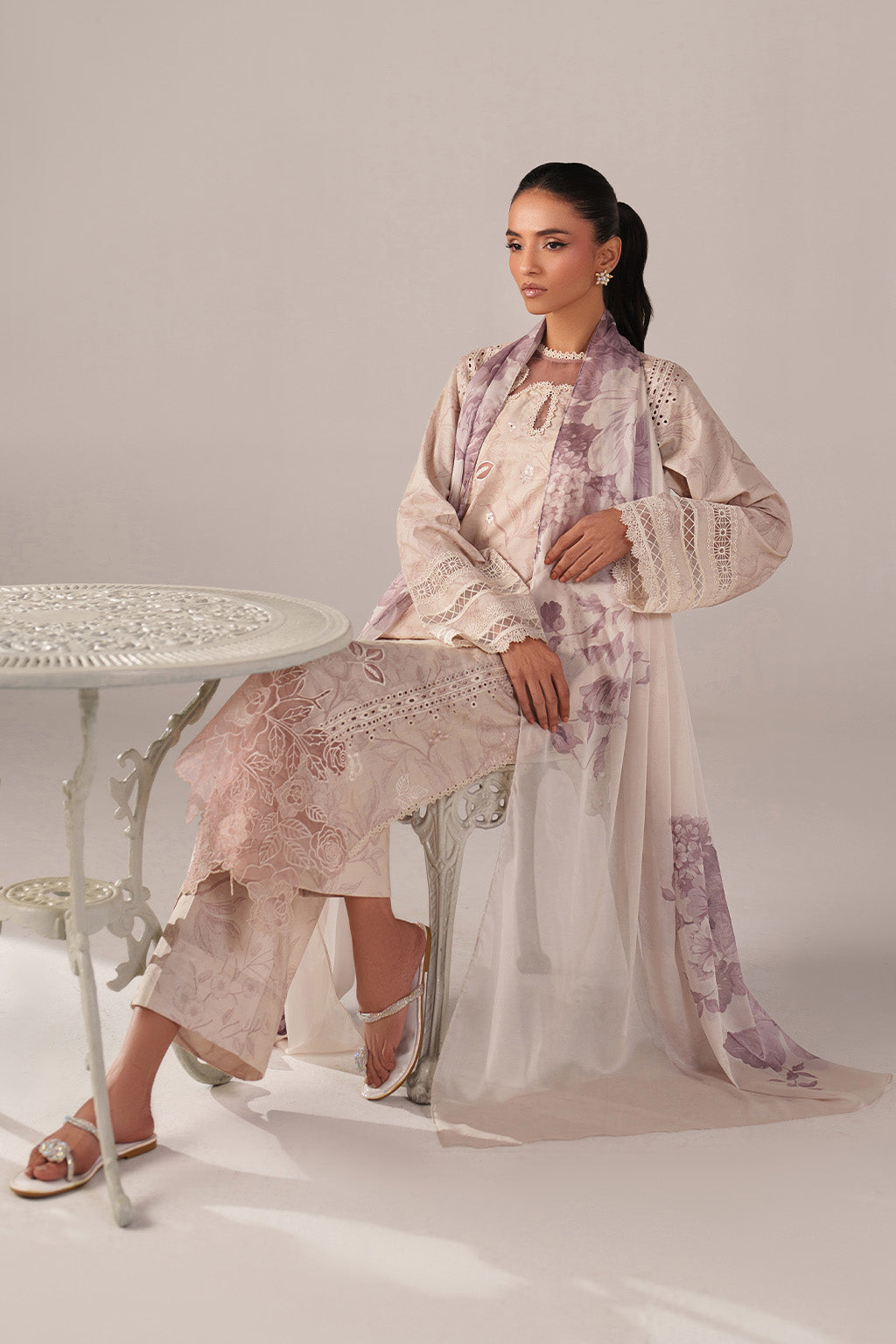 Woman in a floral outfit standing next to a white table on a plain background