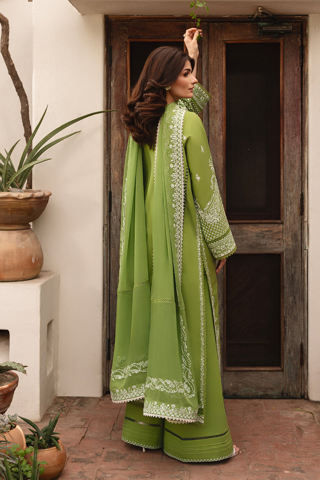 Woman in a green traditional outfit standing in front of a wooden door.