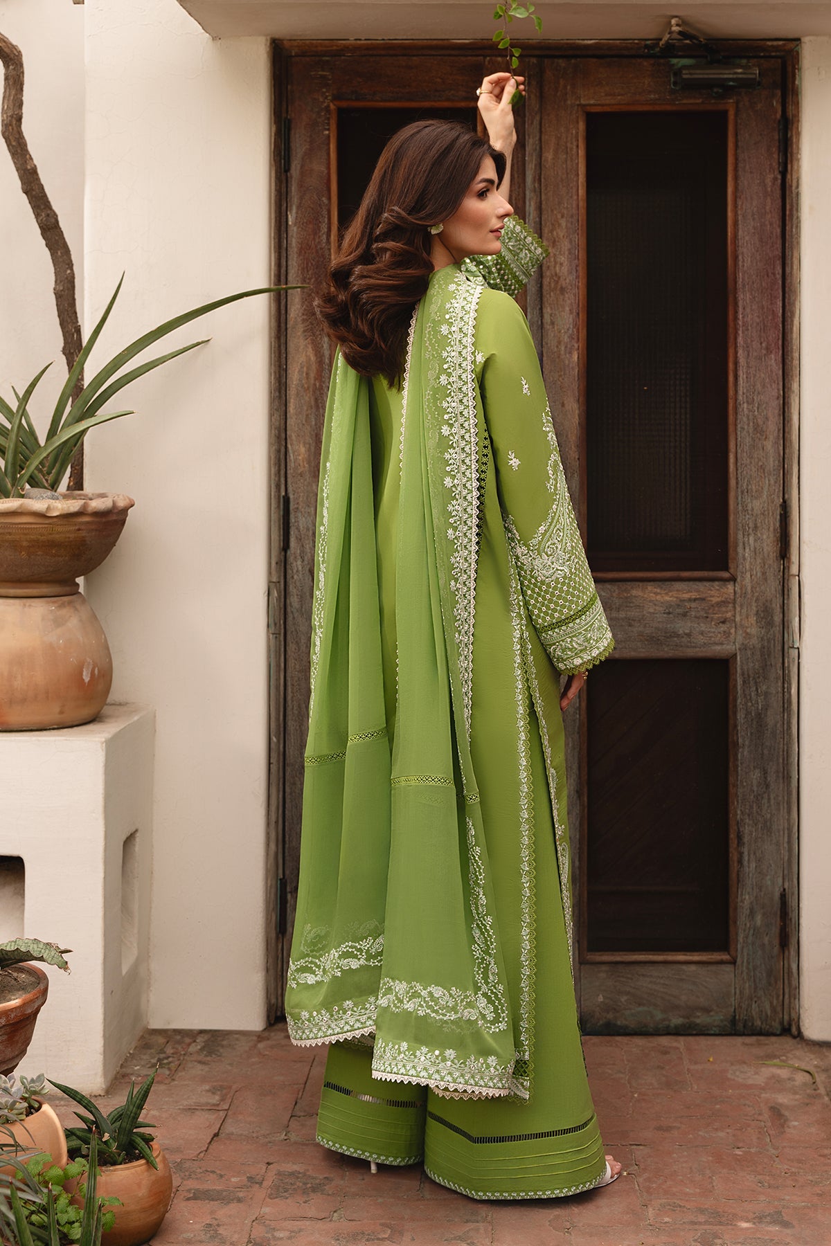 Woman in a green traditional outfit standing in front of a wooden door.