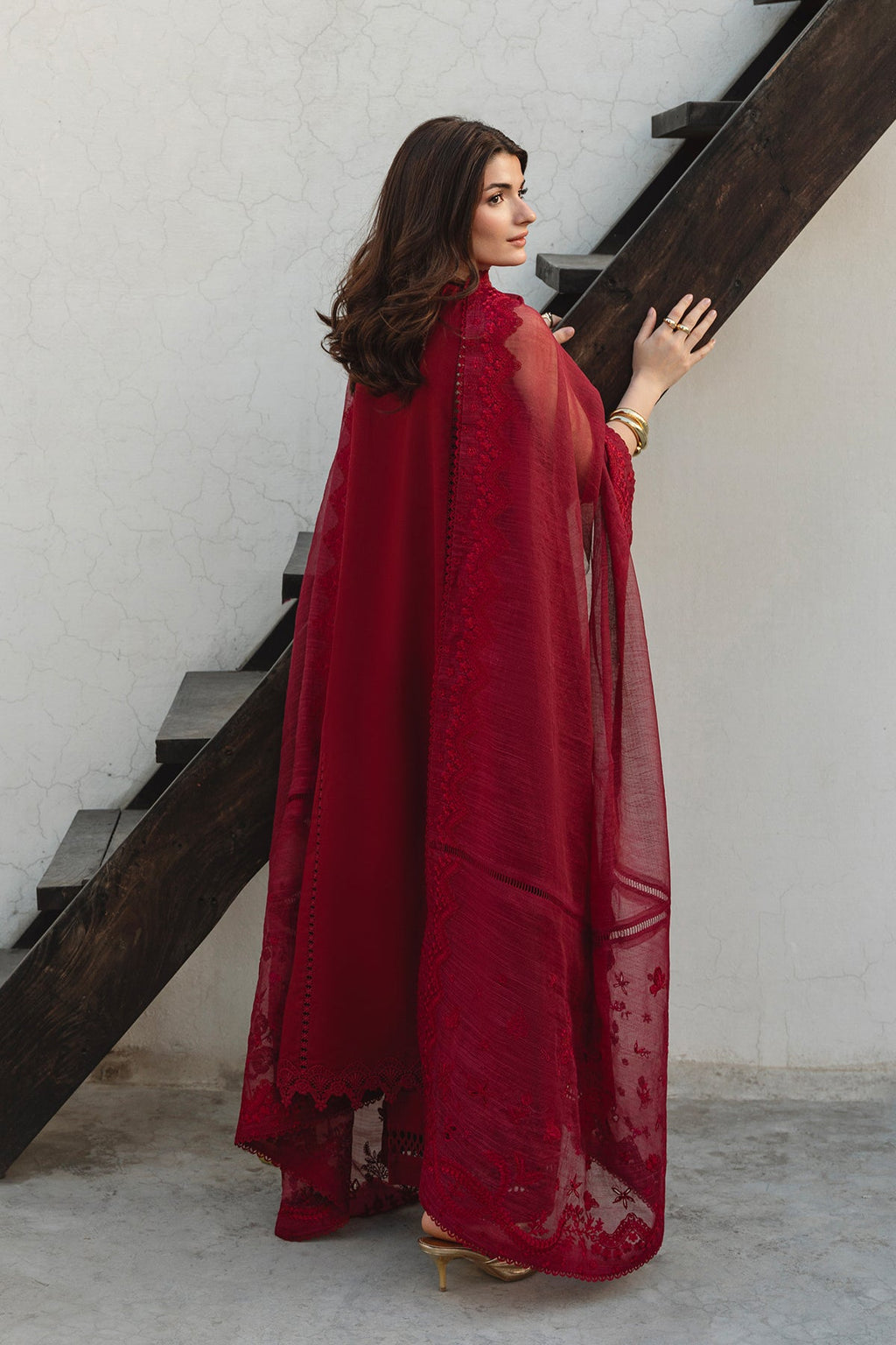 Woman in a red outfit standing on a staircase with a white wall background