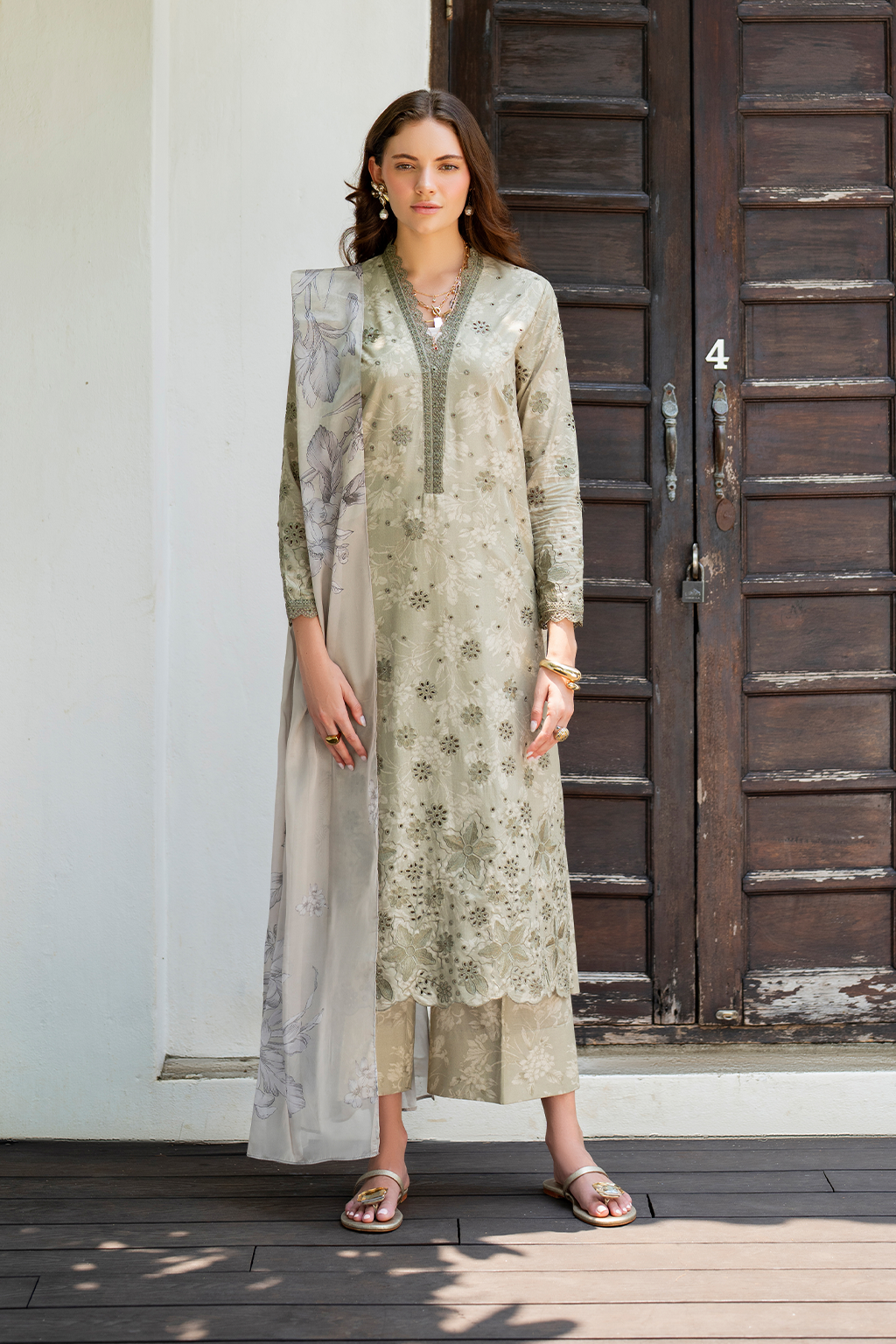 Woman wearing a light green floral dress with a matching dupatta in front of a wooden door.
