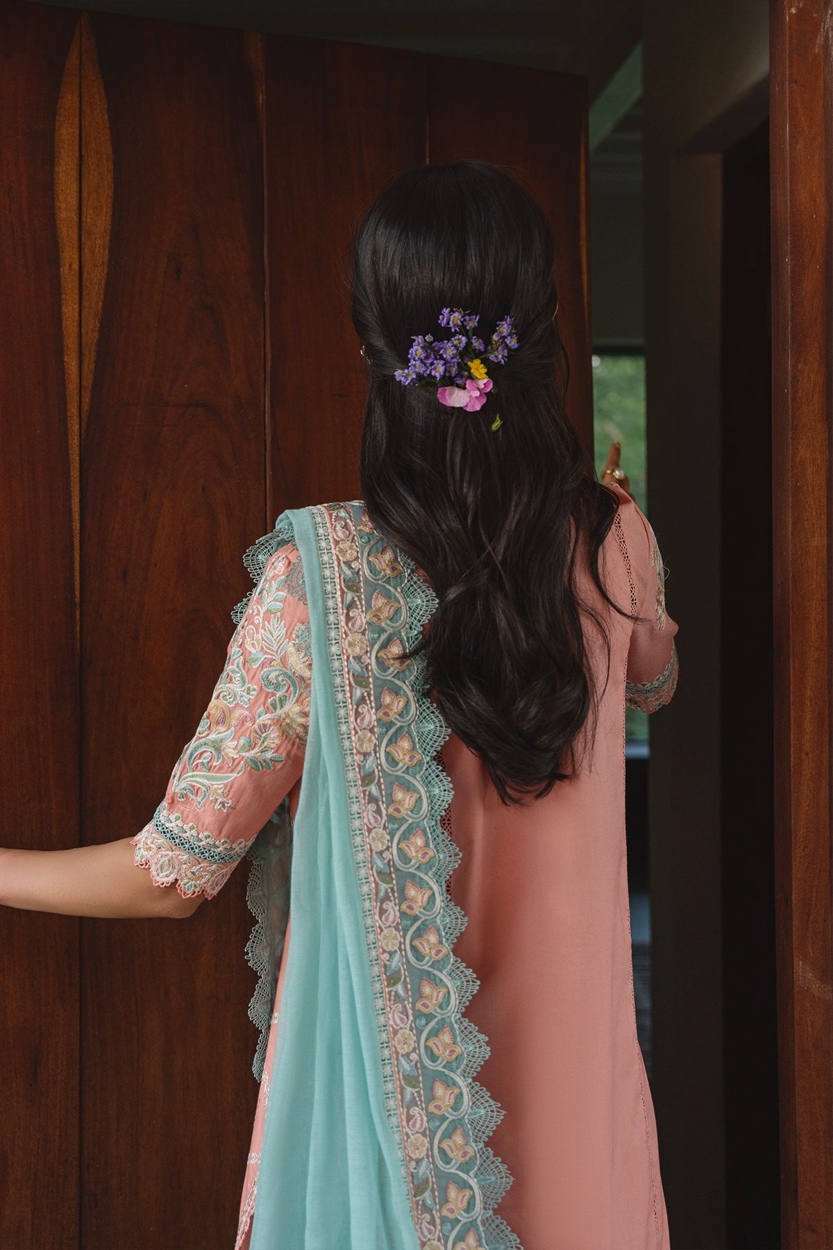 Woman wearing a traditional outfit with a floral hair accessory, standing in front of a wooden door.